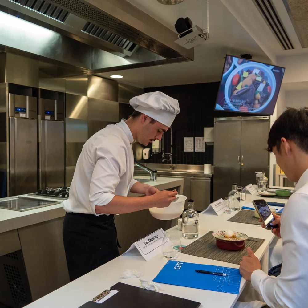 Un alumno presenta su plato al jurado en la cocina.