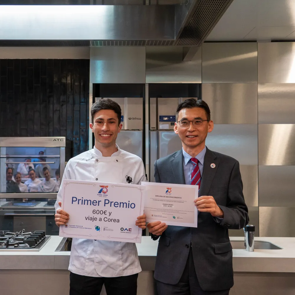 El alumno ganador posa con el diploma junto al Cónsul en la cocina.