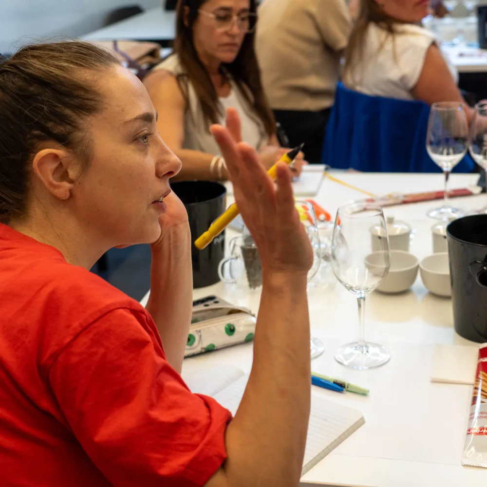 Una alumna levantando la mano para preguntar ante una mesa con instrumentos para vino