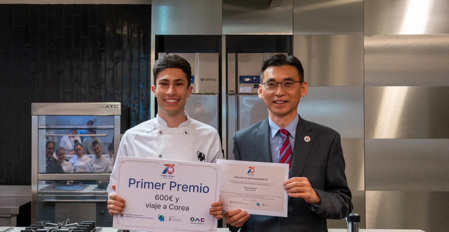 El alumno ganador posa con el diploma junto al Cónsul en la cocina.